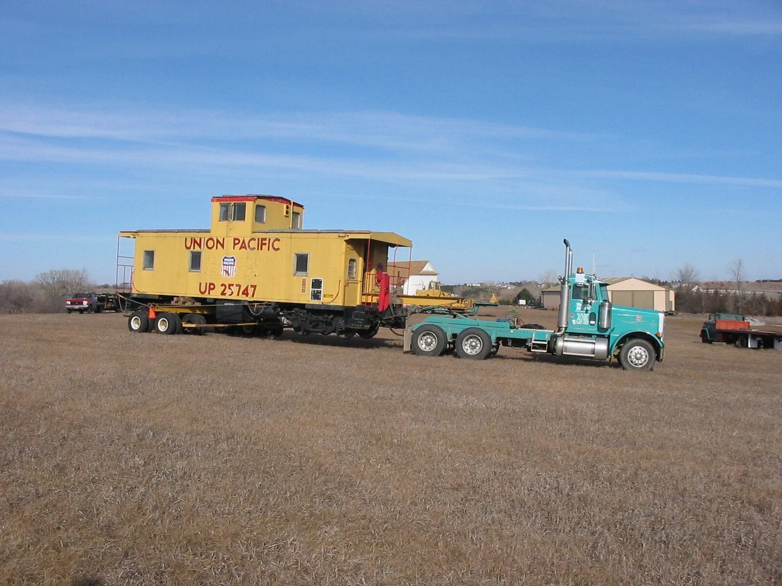 Yellow Union Pacific caboose on a trailer behind a teal truck