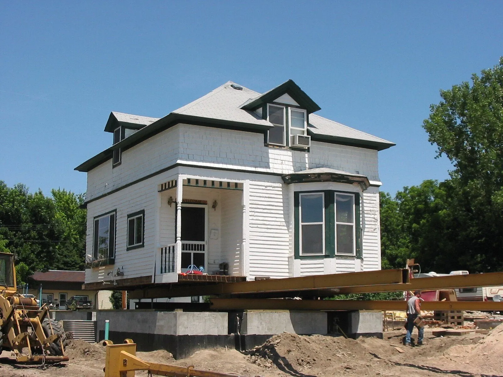 White house with green trim raised on steel beams over a new concrete foundation