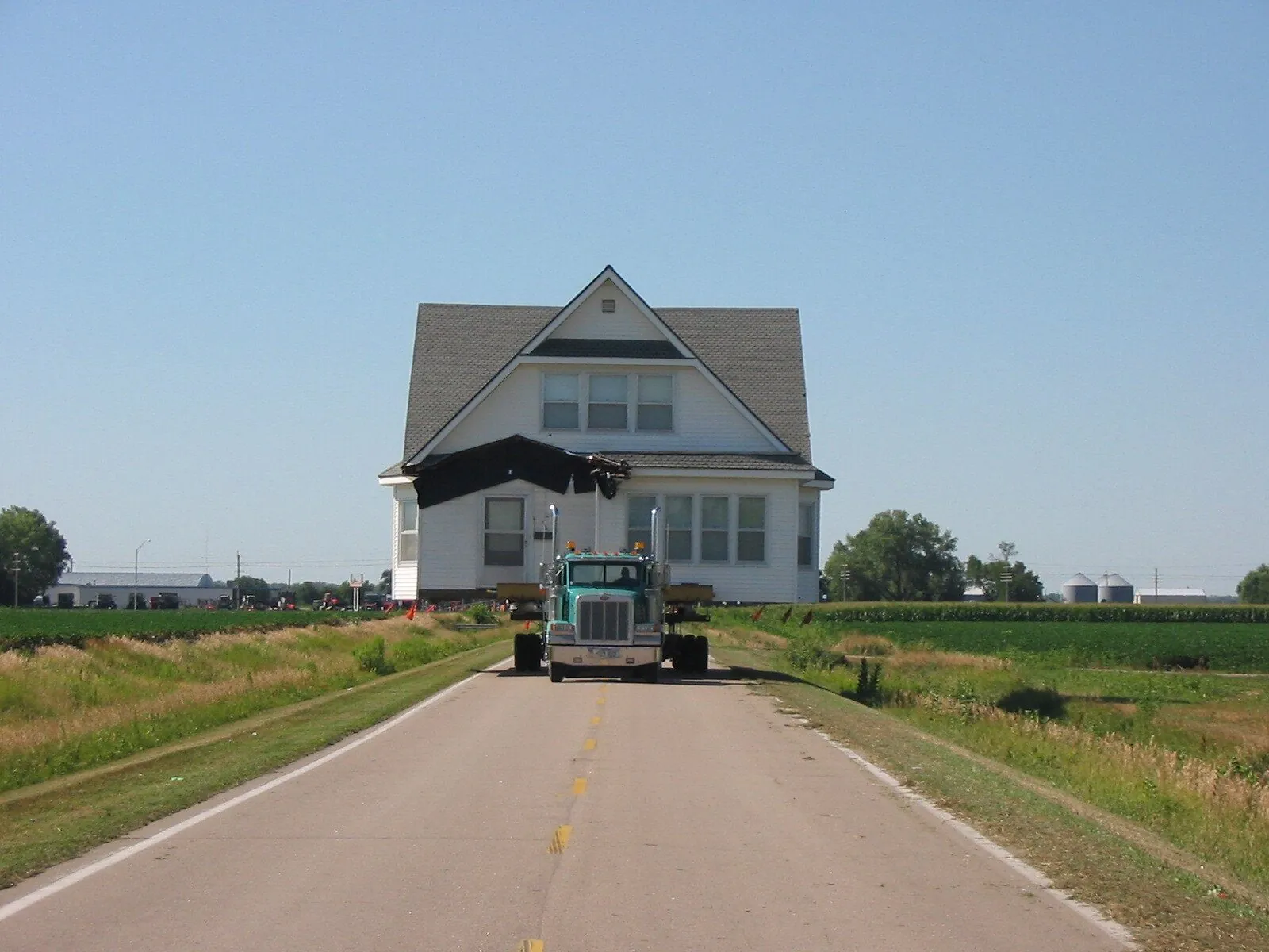 White farmhouse coming head-on down a country road behind a teal truck