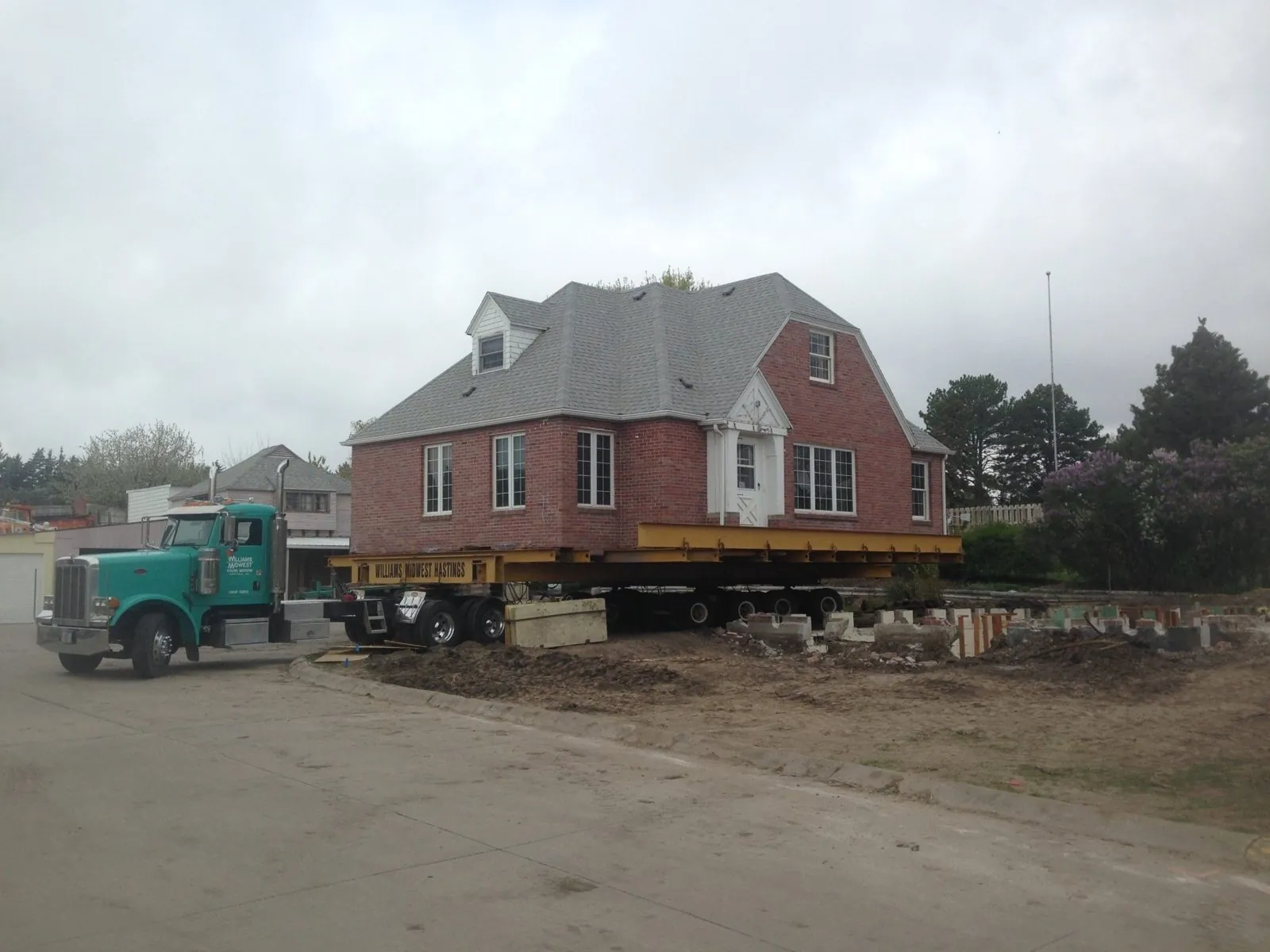 Red brick house on yellow steel beams hitched to a teal truck