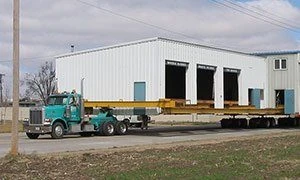 Steel commercial building on a trailer behind a teal truck