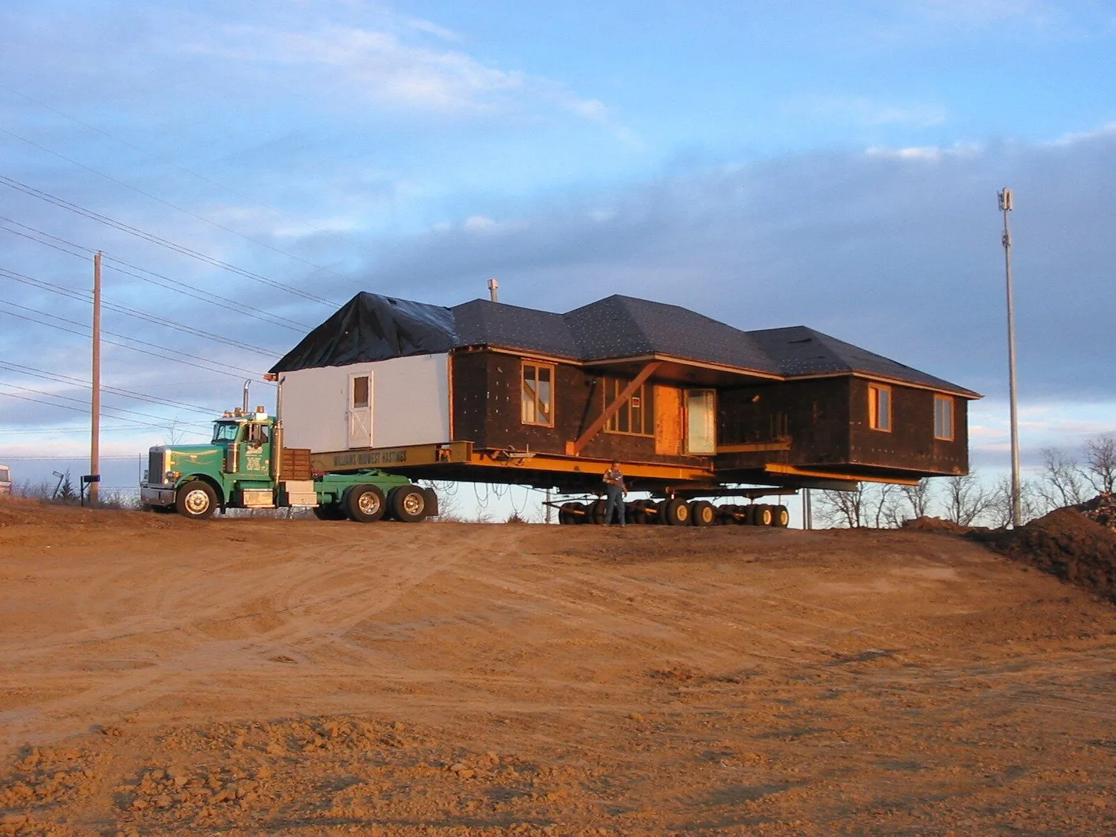 House on steel beams behind a truck on a red dirt site at sunset