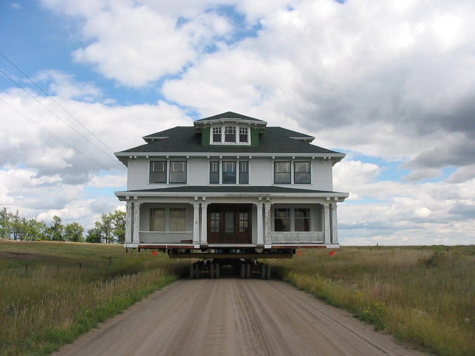 A two-story foursquare house with a front porch coming head-on down a gravel road under a cloudy sky